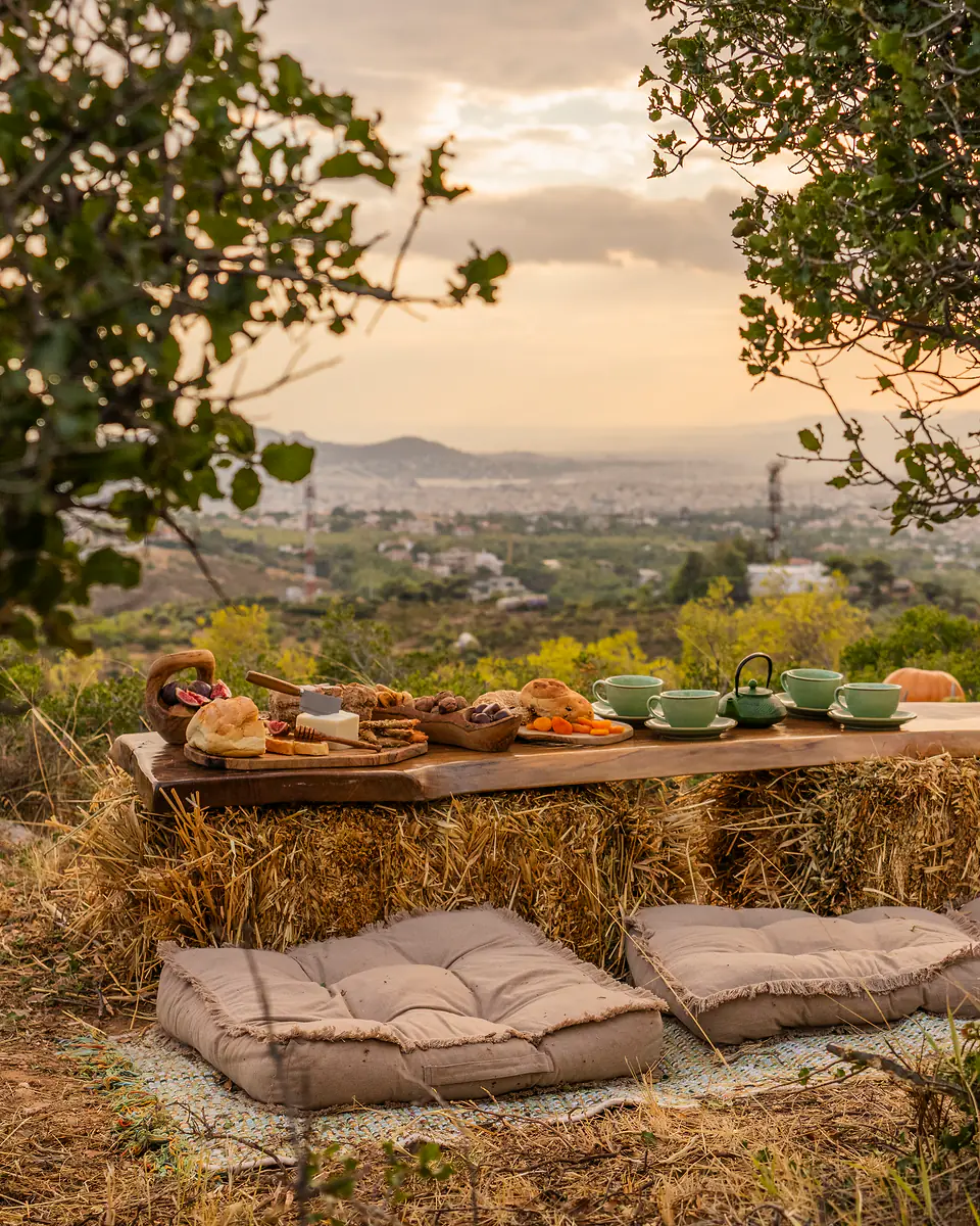 Ξύλινο τραπέζι πάνω σε δέματα άχυρου, με μαξιλάρια στο έδαφος, στημένο στο βουνό την ώρα του ηλιοβασιλέματος